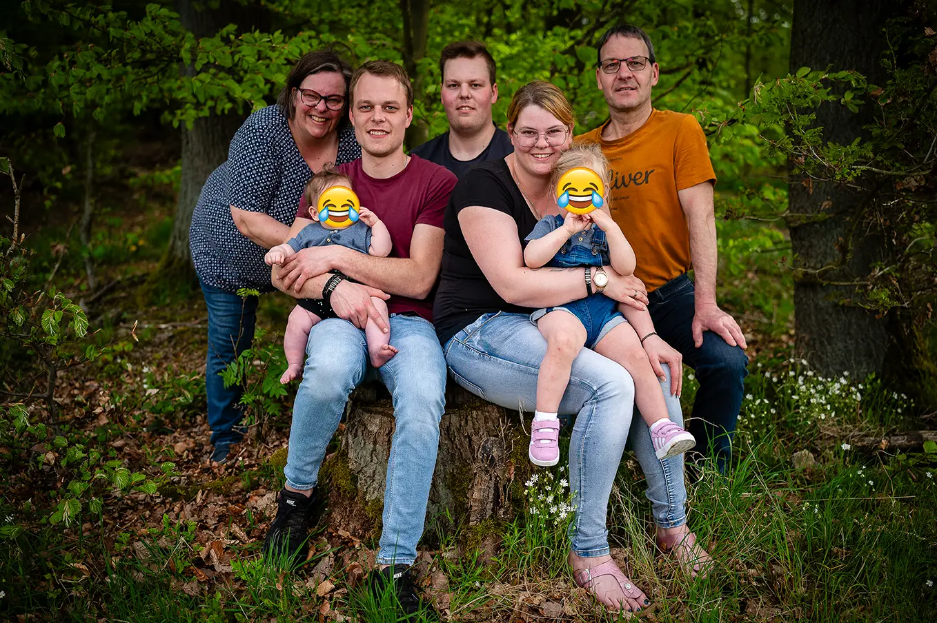 Familie sitz auf einer Wurzel im Wald und schaut in die Kamera