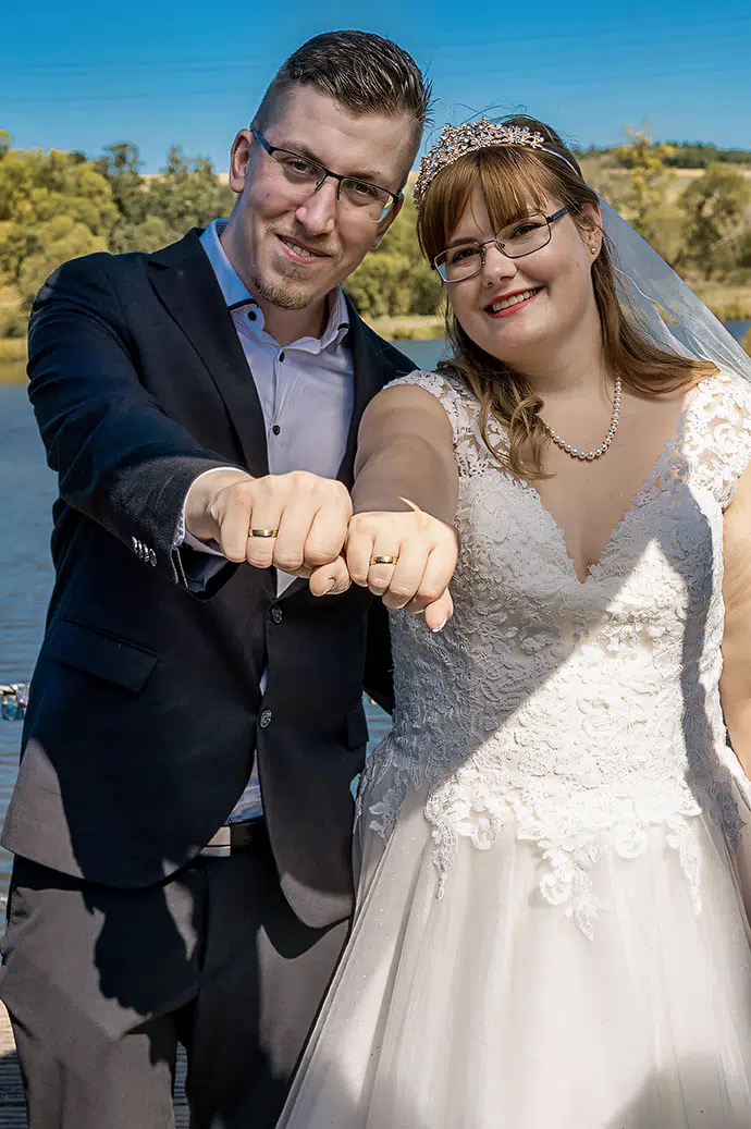brautpaar hält am see ihre getragenen ringe vor die kamera