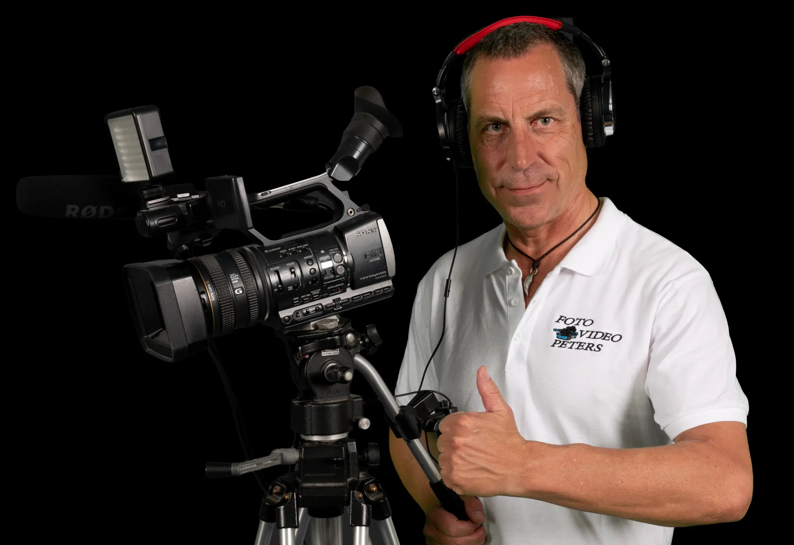ralf peters von foto-video-peters an der videokamera mit kopfhörer und daumen hoch im fotostudio.