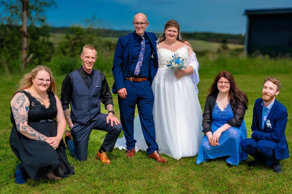 hochzeitspaar mit tGästen auf gruener wiese,